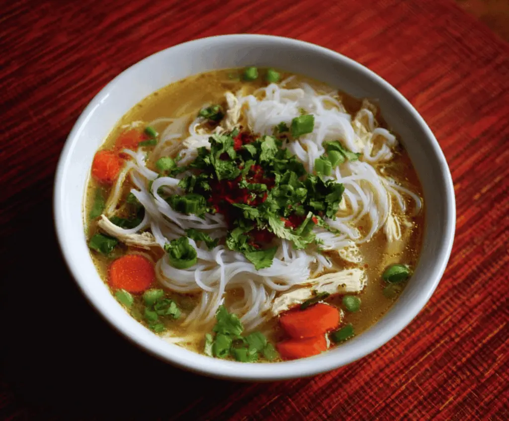 A steaming bowl of Chicken Rice Noodle Soup with tender chicken, rice noodles, fresh herbs, and vegetables in a flavorful broth