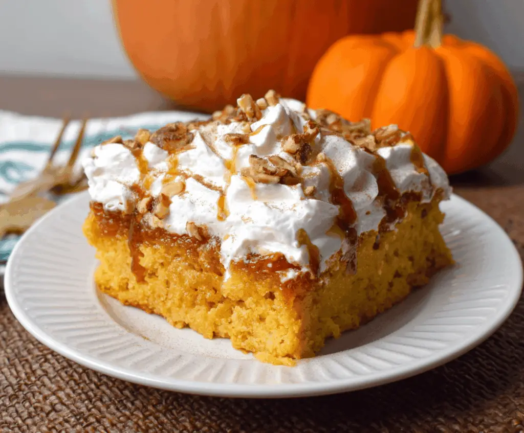 Delicious Pumpkin Poke Cake topped with whipped cream and cinnamon, perfect for fall desserts.