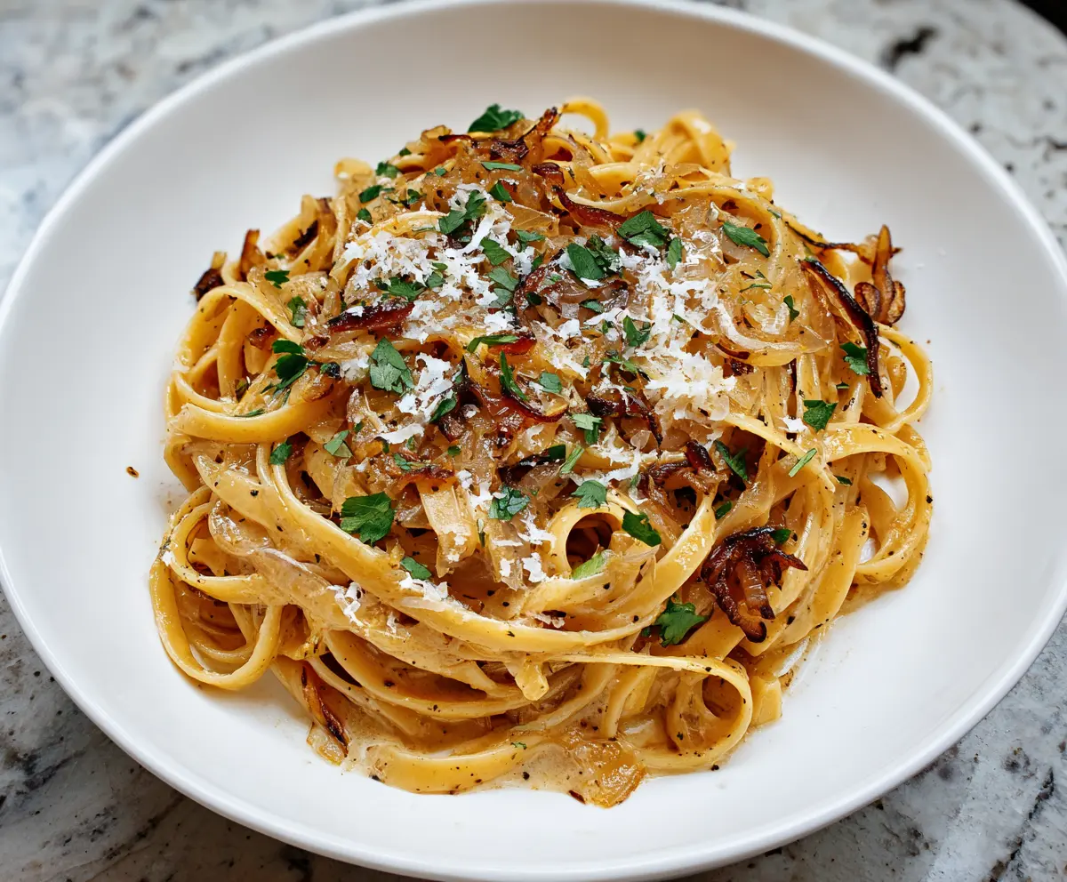 Delicious caramelized onion pasta served on a plate, garnished with fresh herbs.