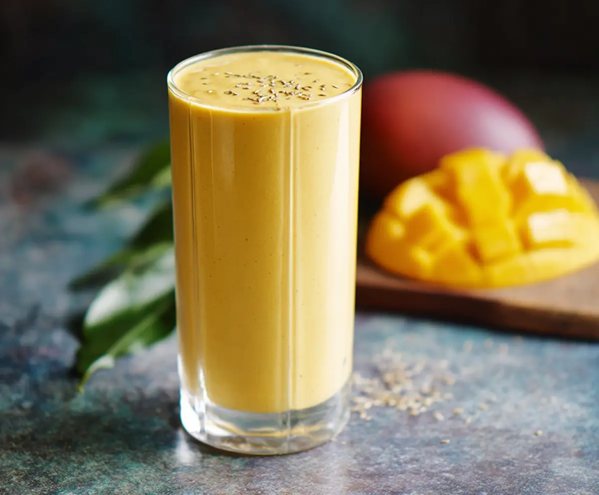 Vibrant mango protein smoothie in a glass, topped with fresh fruit and mint, healthy and delicious drink for breakfast or snack.