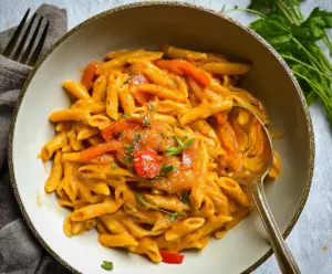 Colorful sweet pepper pasta dish with vibrant red, yellow, and green peppers garnished with fresh herbs.