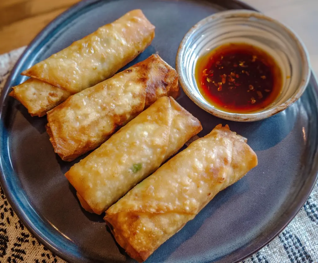 Crispy chicken lumpia served with dipping sauce on a white plate, perfect appetizer for parties.