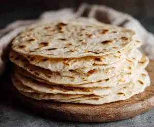 Homemade sourdough discard tortillas stacked on a wooden surface, showcasing their soft texture and golden edges.